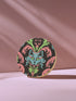 Circular ceramic coaster featuring a turquoise cat face with green eyes on black background, surrounded by pink scrollwork and green leaves in Victorian damask style.
